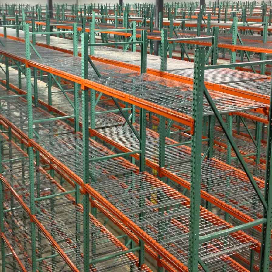 Green and orange pallet racking bays stand tall in. a warehouse each one has wire mesh decking